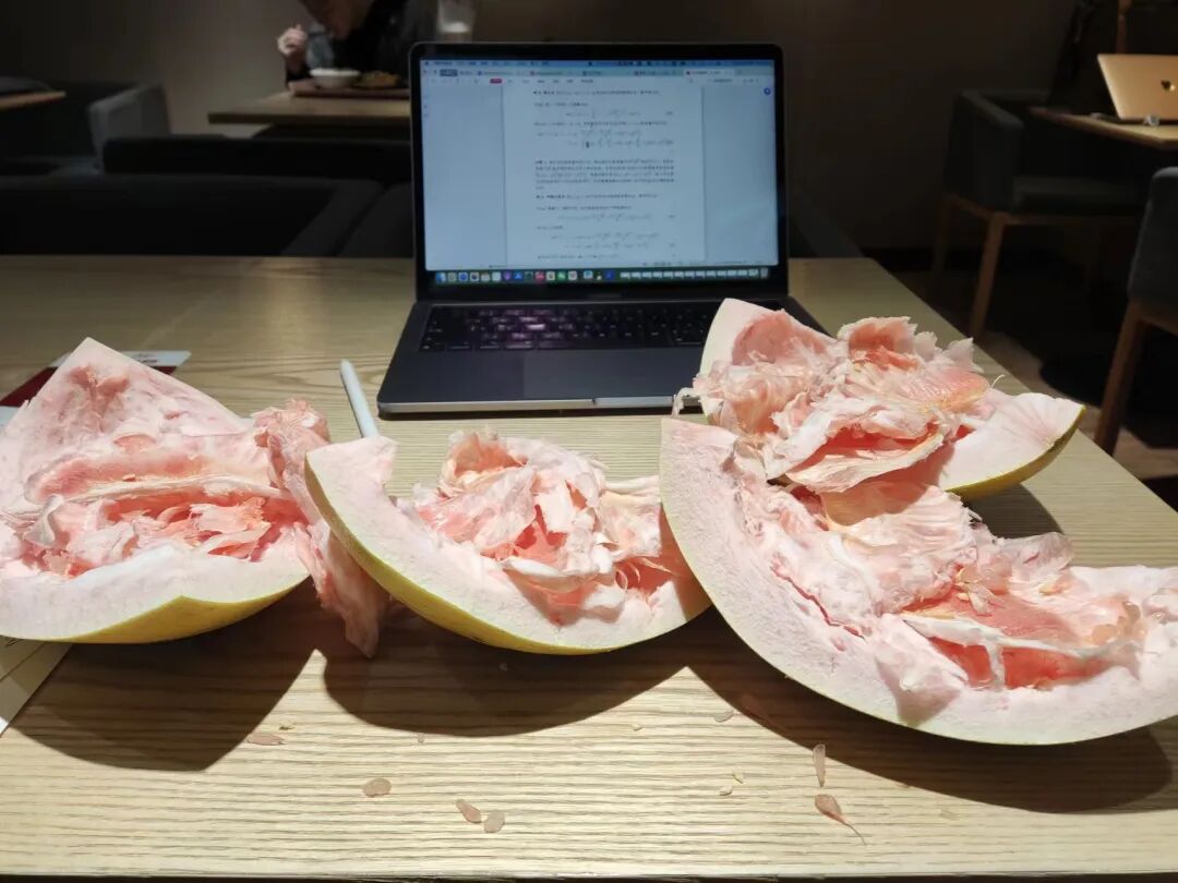 剥开的柚子与桌上打开的 MacBook 并排放置